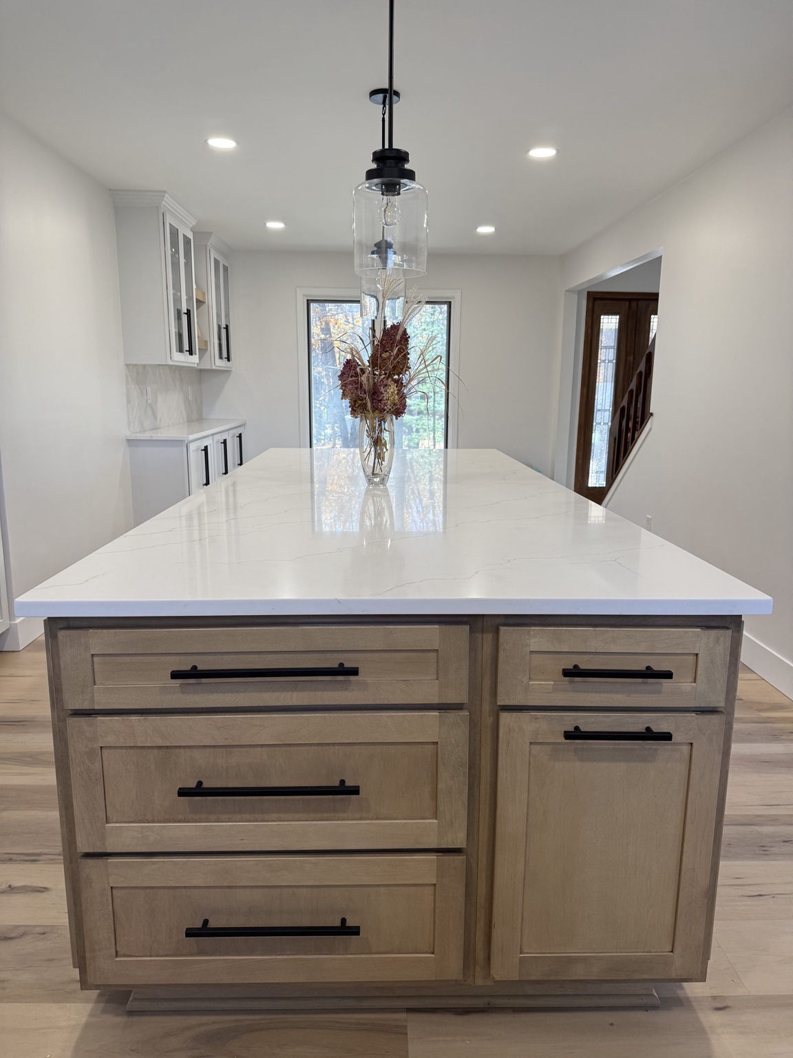 Kitchen with a wood island, quartz countertop, white cabinetry and glass pendant lights